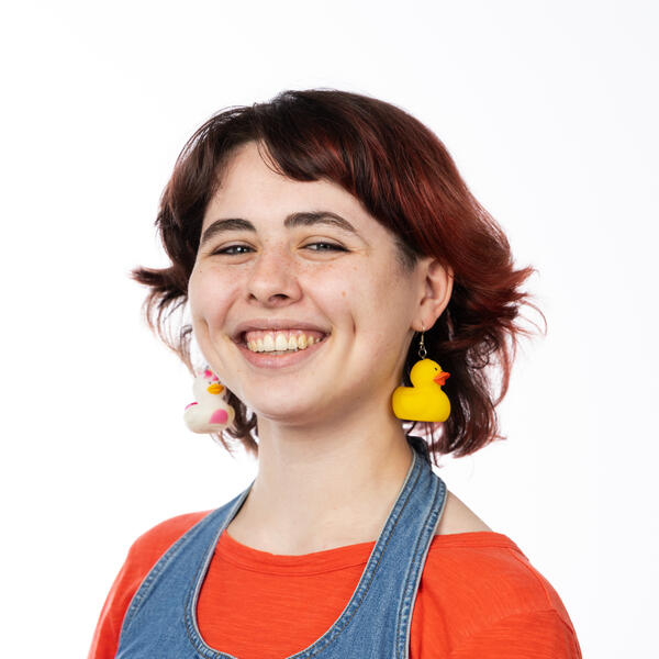 Human with dyed red hair, dimples, and rubber duck earrings.